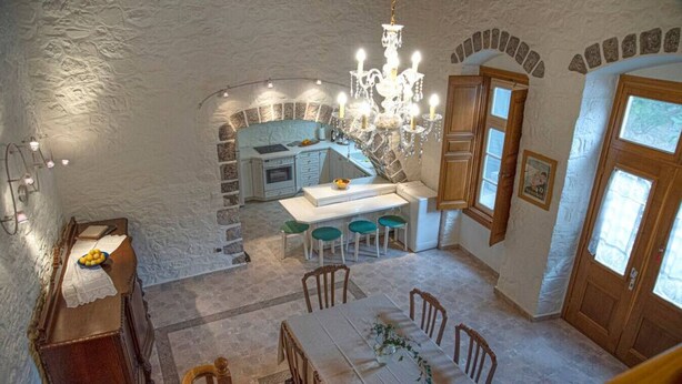 A dining area with a table set for four, a chandelier, and a kitchen in the background.