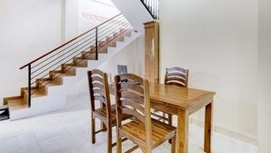 Un intérieur moderne avec un escalier en bois, une table à manger avec des chaises et, par la fenêtre, une vue sur un espace aux motifs rouges.