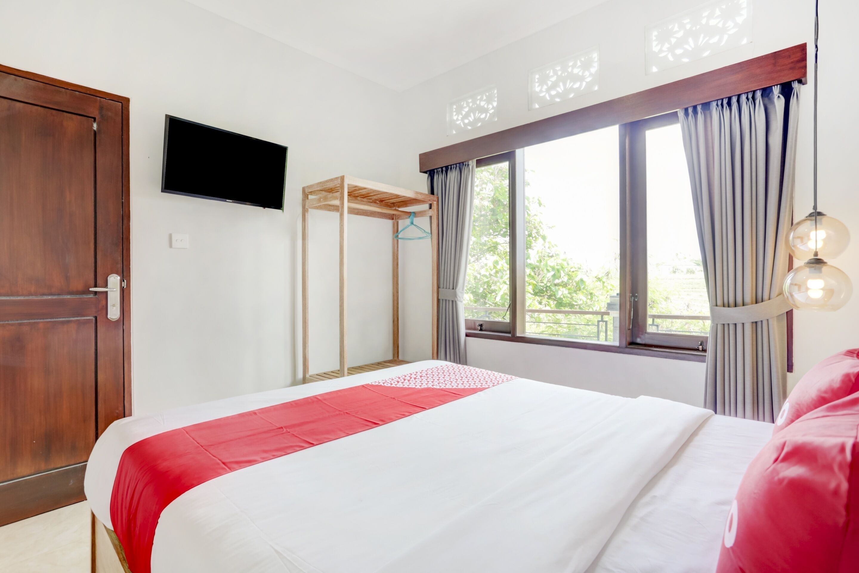 A hotel room with a bed, a TV, a window with curtains, and a wooden door.