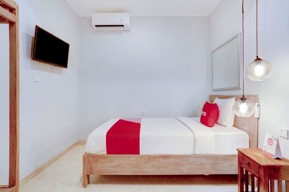 A bedroom with a bed, a bedside table, a wall-mounted TV, an air conditioning unit, and a hanging light fixture.