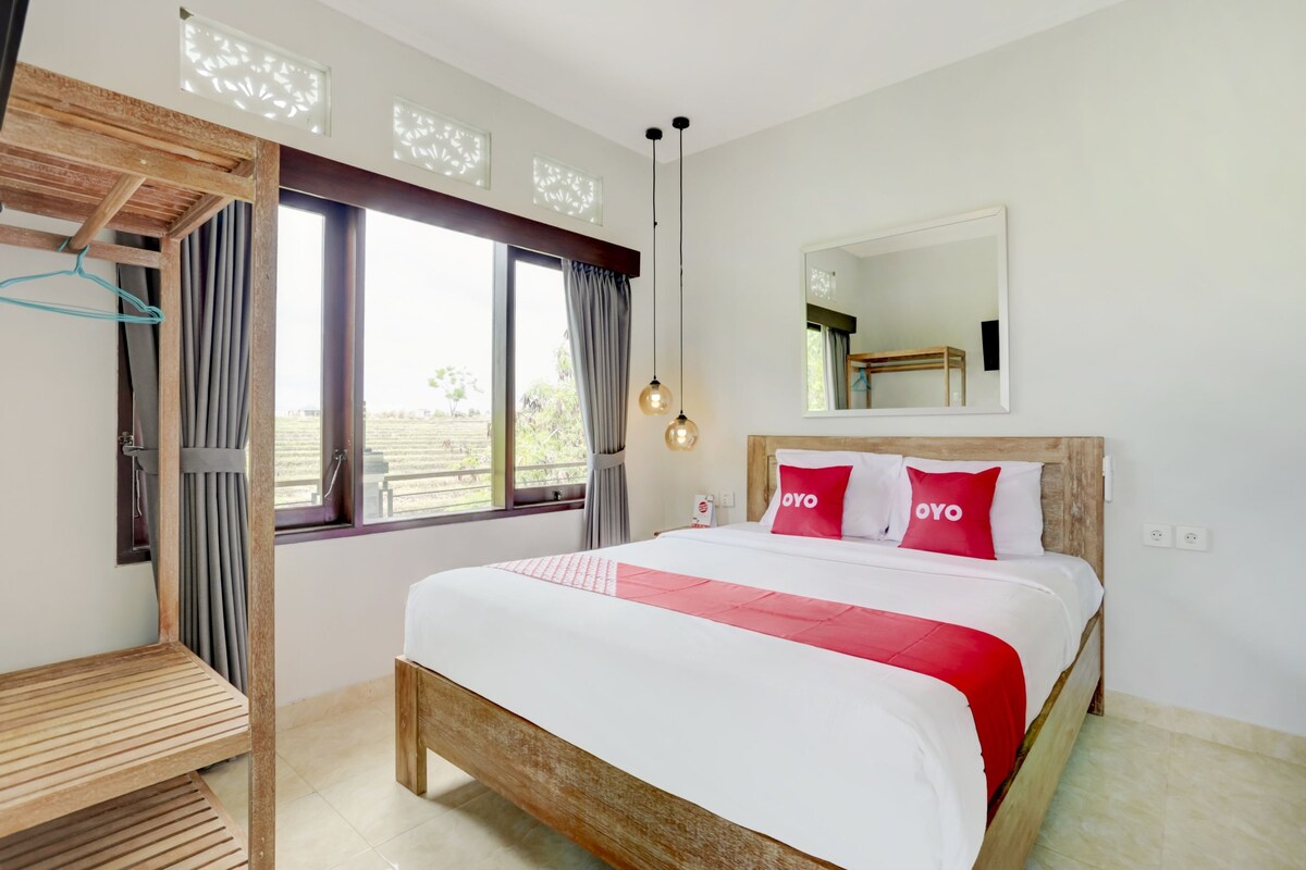 Une chambre d’hôtel avec un lit, une tête de lit en bois, un luminaire suspendu, une fenêtre avec des rideaux et un miroir au mur.