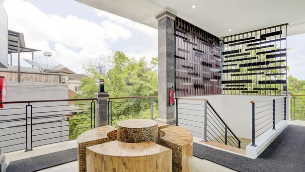 Un espace extérieur moderne, aménagé avec une table ronde en bois et des bancs, un escalier doté d’une rampe en métal, et offrant une vue sur la verdure et les bâtiments en arrière-plan.