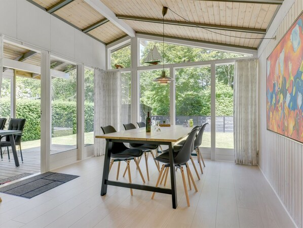A spacious dining area with a large table and chairs, large windows, and a view of the outdoors.