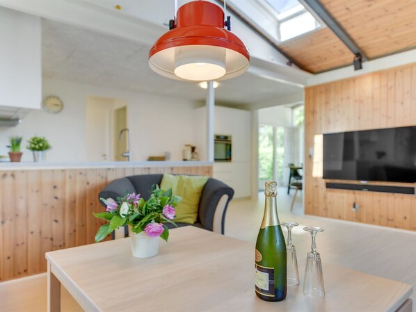 A modern kitchen with wooden cabinets, a dining area with a table, a red pendant light, and a bottle of champagne.