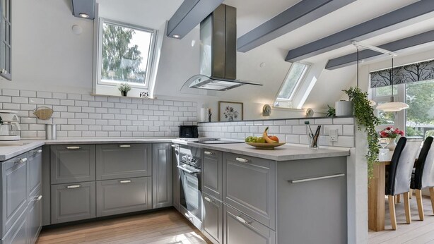 Une cuisine moderne avec des meubles gris, un îlot central et un coin repas comprenant des chaises et une table en bois.