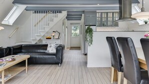 Une cuisine moderne dotée d’un îlot central, un coin repas avec des chaises en cuir noir, un canapé en cuir noir et un escalier menant à un niveau supérieur.