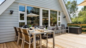 Un patio couvert avec une table et des chaises, de grandes fenêtres et une terrasse en bois.