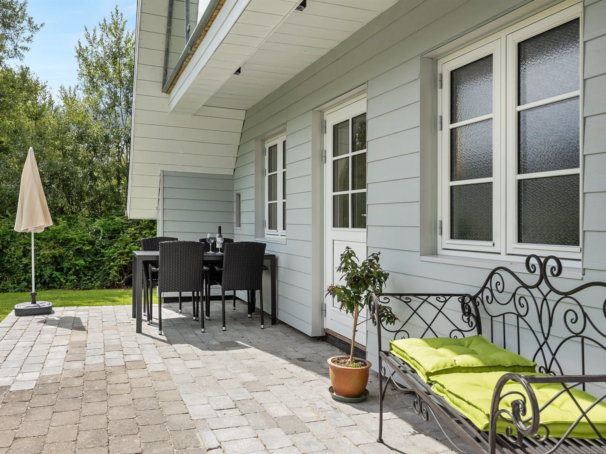 A patio with a table and chairs, a metal bench, a potted plant, and a window with frosted glass.