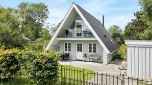 Une maison à deux étages avec un toit en pente, un balcon et une cour clôturée.