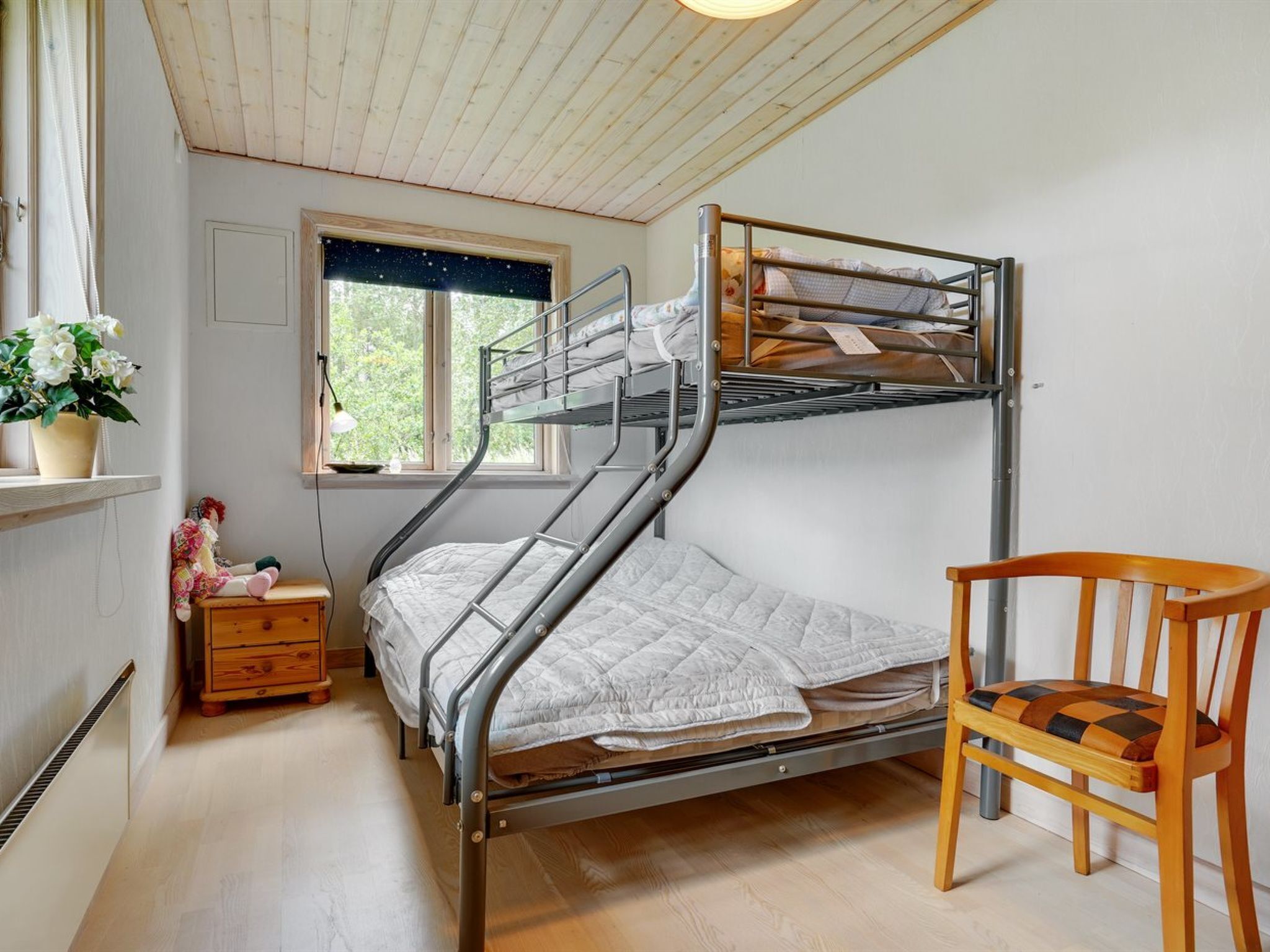 A bunk bed with a desk and chair, a window with a view of trees, and a potted plant.