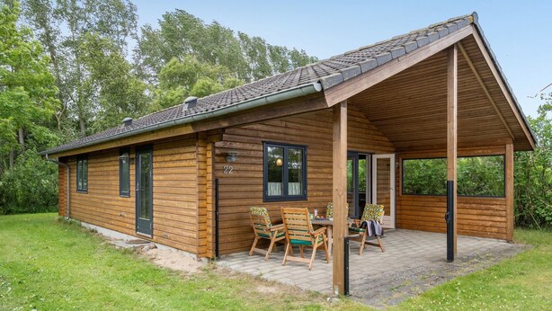 Une cabane en bois dotée d’un patio couvert, d’une table à manger avec des chaises et du chiffre « 22 » peint sur le mur.