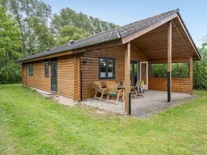 A wooden cabin with a covered patio, a dining table with chairs, and a number '22' on the wall. - "Rəzvan" - 120m from the sea by Interhome (Brenderup Fyn)