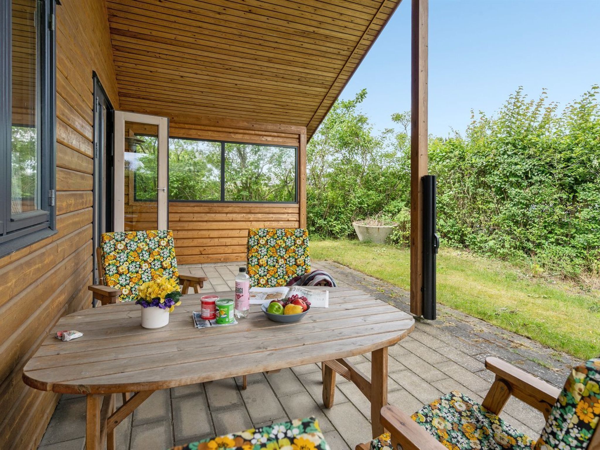 A wooden deck with a table and chairs, surrounded by greenery.