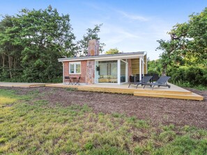 Une maison moderne dotée d’une extension en verre, d’un espace salon extérieur et d’une cheminée en pierre.