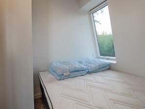 Une petite chambre avec un lit simple, un matelas blanc et une couverture bleue.