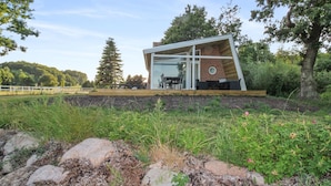 Een modern huis met een glazen gevel, een bakstenen schoorsteen en een terras met buitenmeubilair.