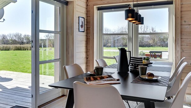Interior de una cabaña de madera con una mesa de comedor, sillas y un ventanal que ofrece vistas al exterior.
