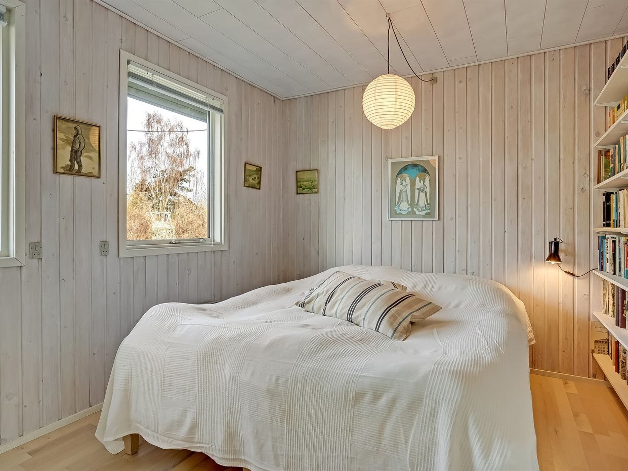 Een slaapkamer met een groot bed, houten wanden, een raam en een boekenkast.