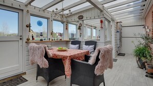 Ein Wintergarten mit Esstisch, Stühlen und einer Pendelleuchte.