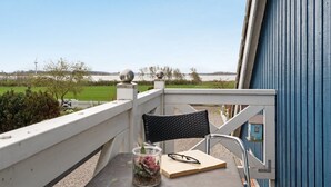 Ein Balkon mit Blick auf ein grünes Feld und Windkraftanlagen, ein Stuhl, ein kleiner Tisch mit einem Glas und einem Buch sowie ein blauer Geländer.