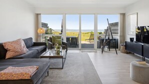 A modern living room with a grey sofa, a coffee table, and a TV. There is a large window with a view of the beach. - "Ninne" - 50m from the sea by Interhome (Assens)
