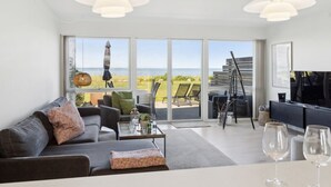 A modern living room with a sofa, coffee table, and a dining area with a TV. Large windows offer a view of the sea and outdoor seating. - "Ninne" - 50m from the sea by Interhome (Assens)