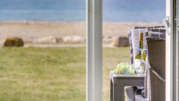 A table with a bottle of wine, a glass, and grapes, overlooking a beach with the ocean in the background. - "Ninne" - 50m from the sea by Interhome (Assens)