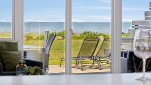 A room with large windows overlooking a beach and the sea. There are two chairs and a table with a glass of wine. - "Ninne" - 50m from the sea by Interhome (Assens)