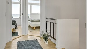 A modern interior with a wooden floor, a staircase with a black railing, and a bed with a view of the sea through large windows. - "Ninne" - 50m from the sea by Interhome (Assens)