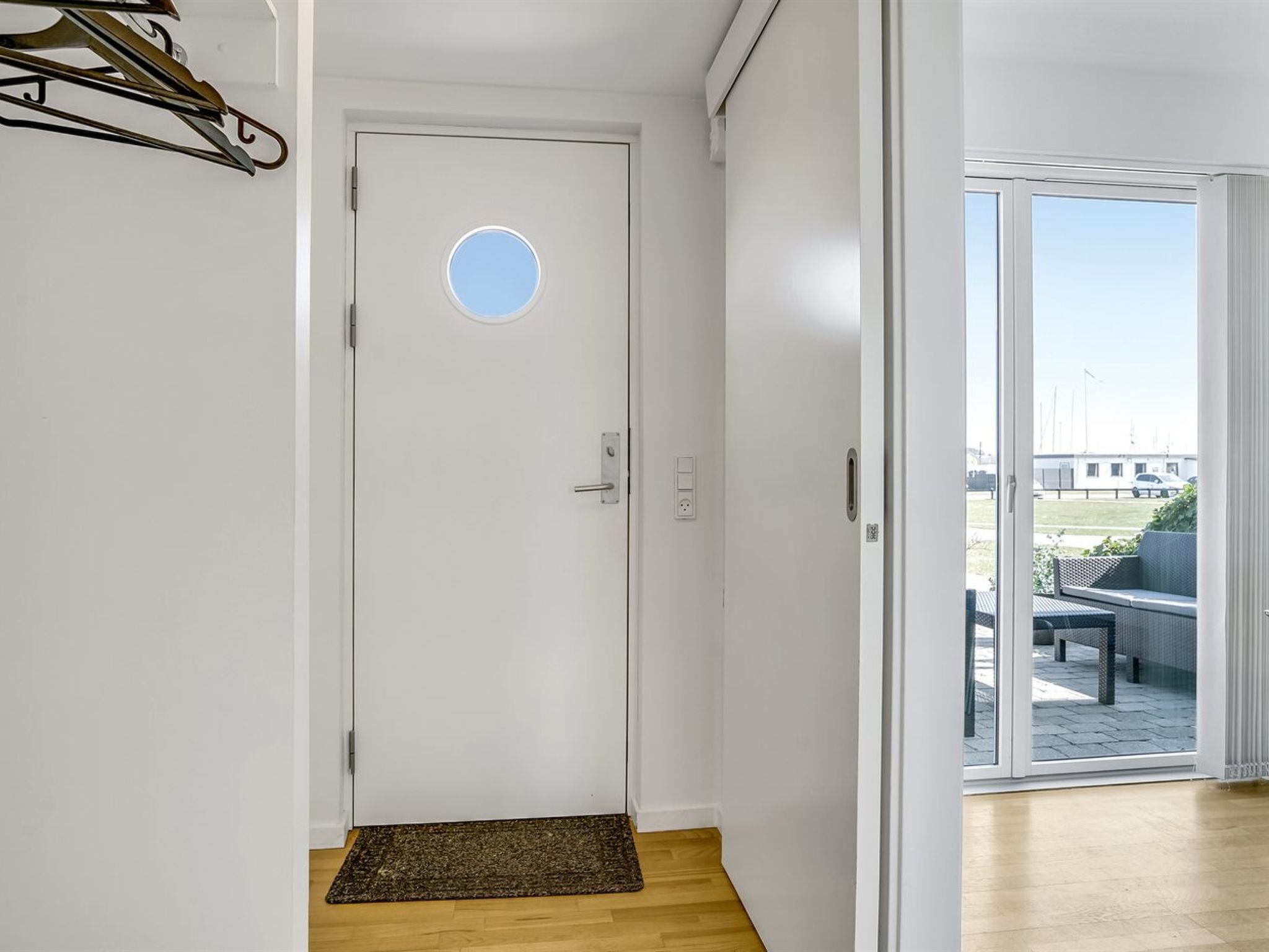 Una puerta blanca con un ventanal circular, un felpudo y un suelo de madera.