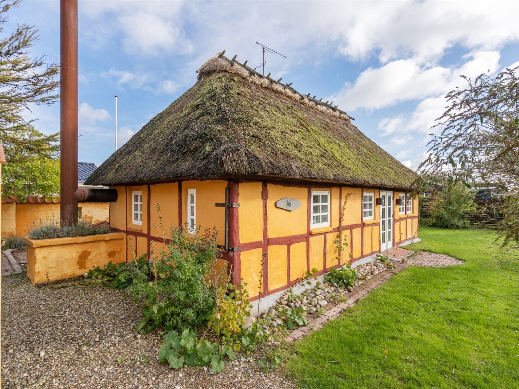 A traditional thatched-roof house with a number '16' sign, surrounded by a well-maintained garden and a gravel path.