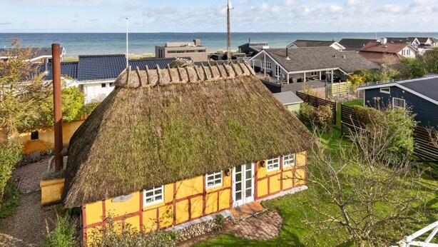 Ein traditionelles gelbes Haus mit Strohdach, umgeben von einem gepflegten Garten und Blick auf das Meer.