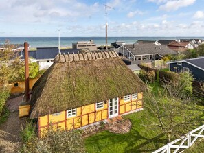 Ein traditionelles gelbes Haus mit Strohdach, umgeben von einem gepflegten Garten und Blick auf das Meer.