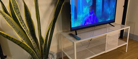 A television on a white stand with a plant beside it.