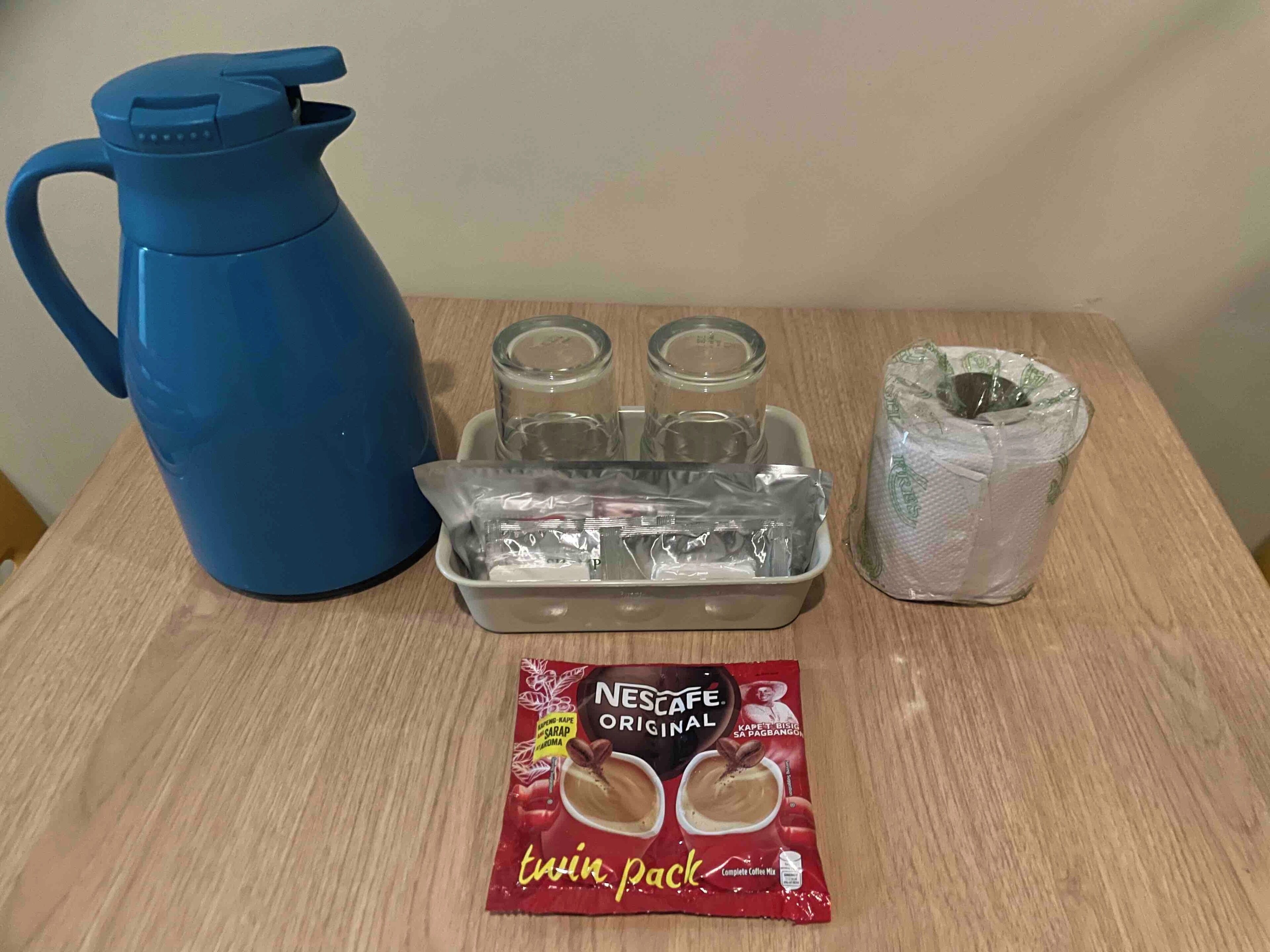 Eine Kaffeemaschine, zwei Gläser, ein Sachet Sahne und ein Zuckerbehälter auf einem Holztisch.