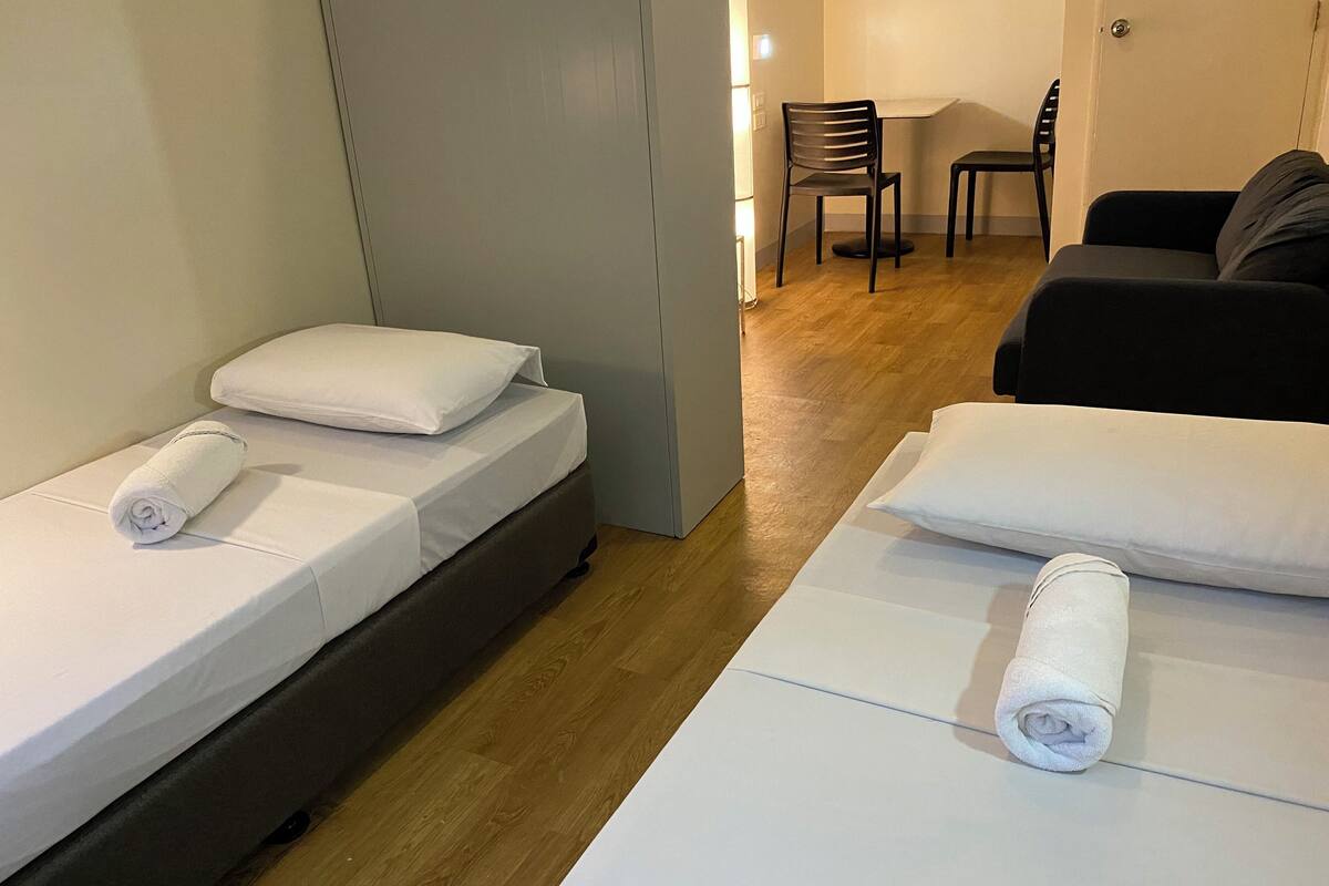 A hotel room with two single beds, a sofa, a chair, and a wooden floor.