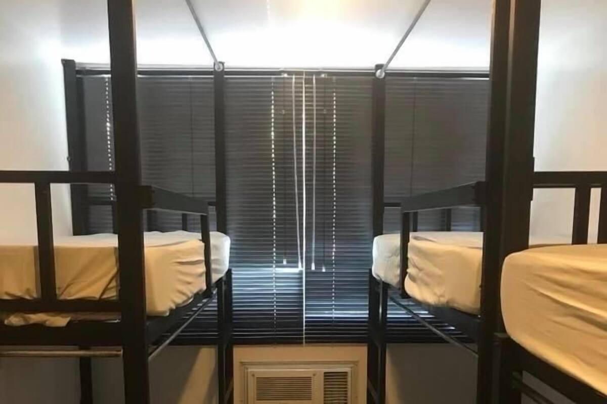 A bunk room with two beds, a window with blinds, and a wall-mounted air conditioning unit.