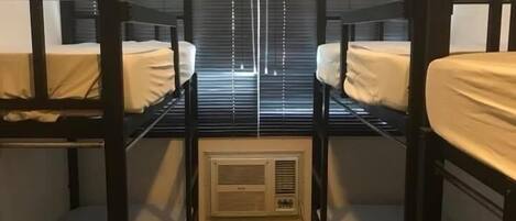 Une chambre avec deux lits superposés, une fenêtre avec des stores et un climatiseur fixé au mur.