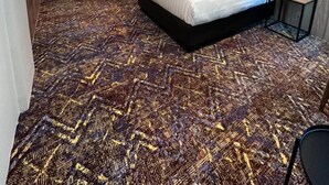 A hotel room with two beds, a patterned carpet, a grey textured wall, and a small side table. - Le'genda Hotel (Kajang)