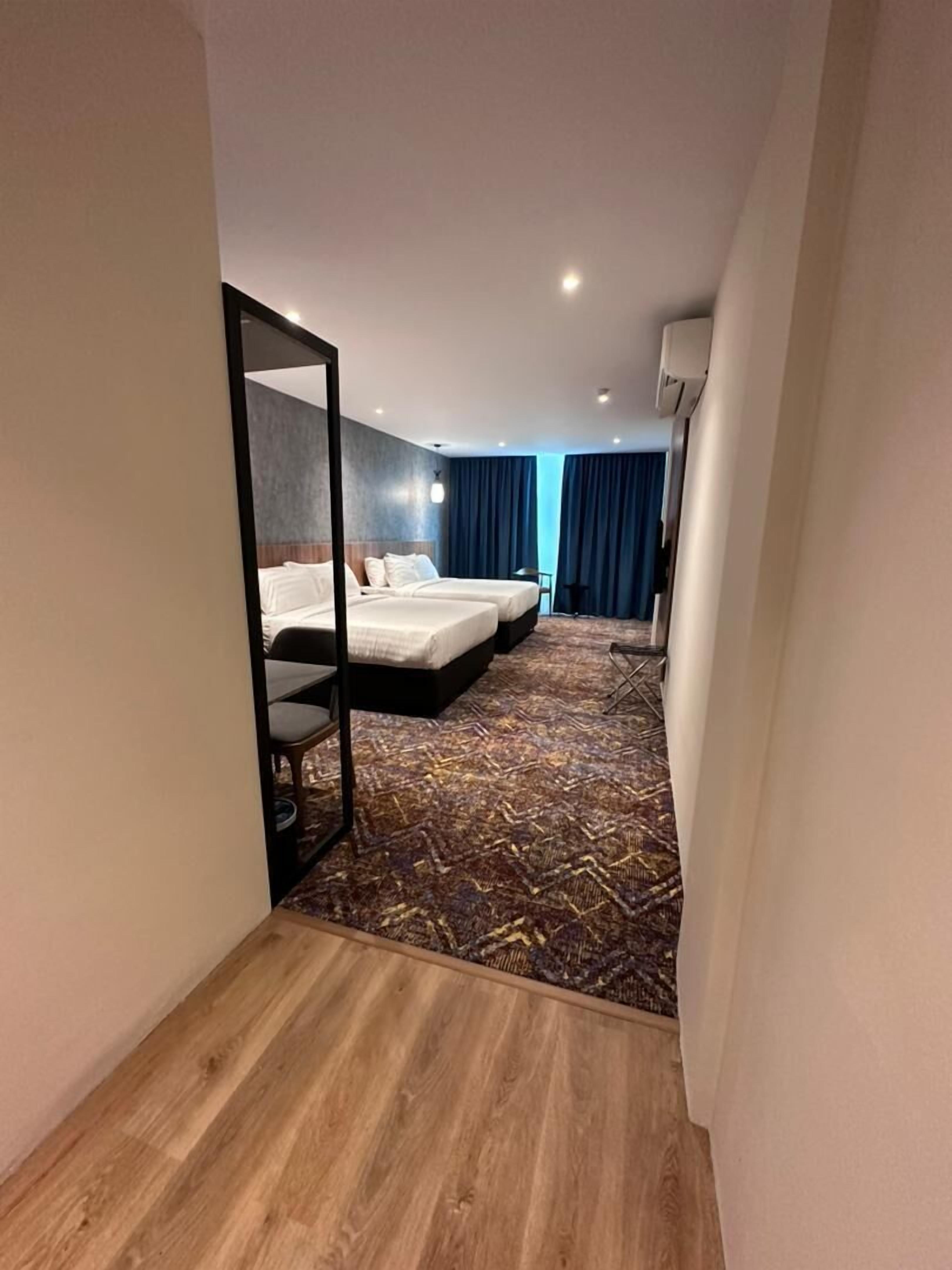 Une chambre d’hôtel avec deux lits, un miroir, un plancher en bois et une moquette à motifs.
