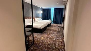 A hotel room with two beds, a mirror, a wooden floor, and a patterned carpet.