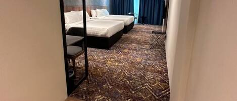 Habitación de hotel con dos camas, un espejo, suelo de madera y alfombra estampada.