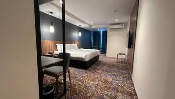Una habitación de hotel moderna con una cama grande, un escritorio con silla, una mesita y un espejo.
