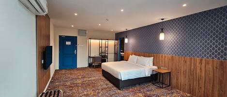 A hotel room with a bed, a desk, a chair, an air conditioning unit, and a blue door.