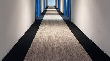 Un pasillo largo y estrecho con suelo alfombrado y puertas azules a ambos lados.
