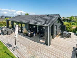 Een modern terras buiten met een overdekte patio, voorzien van tafels, stoelen en een barbecue.