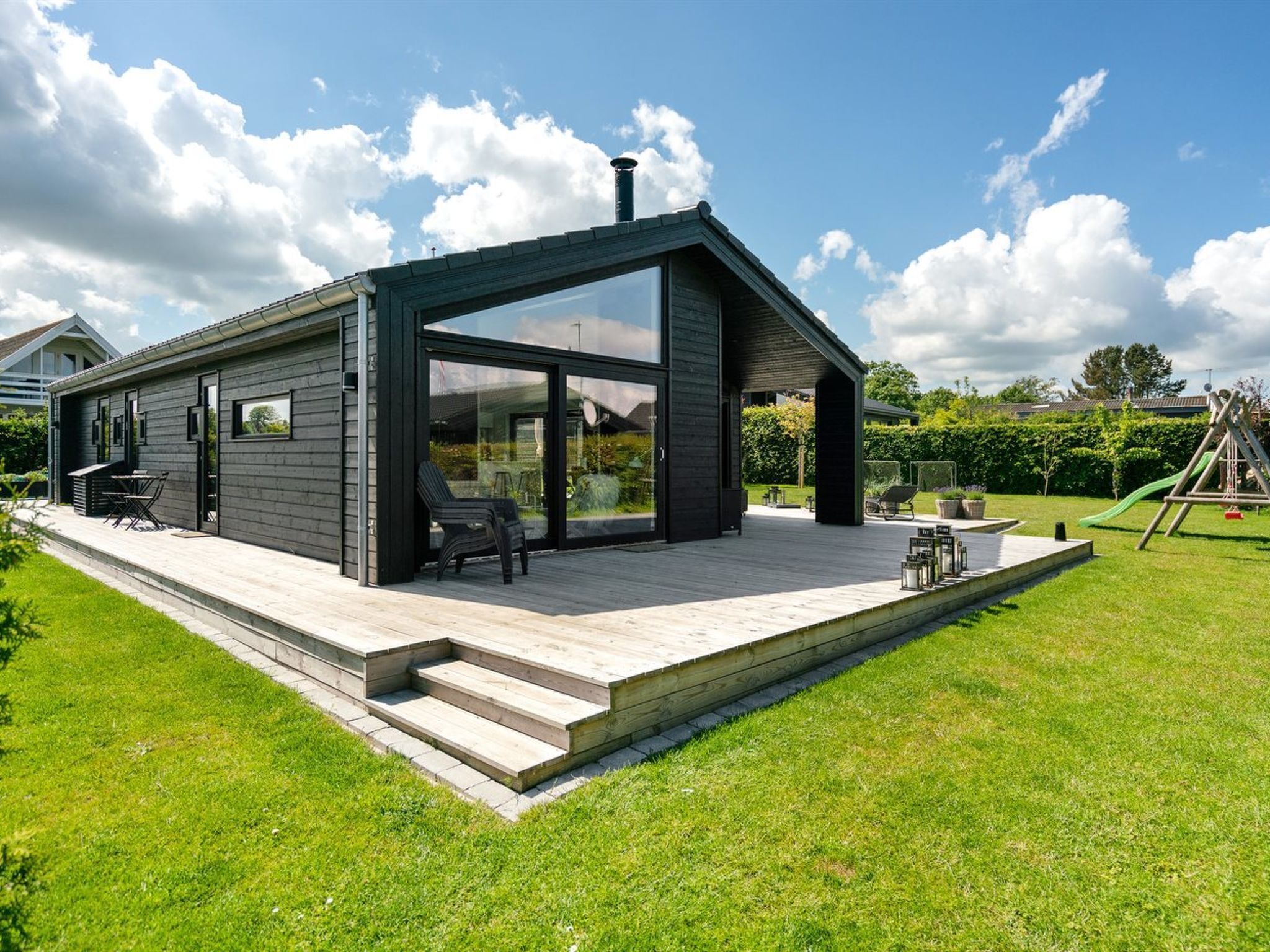 A modern house with a large glass door, a wooden deck, and a grassy yard.