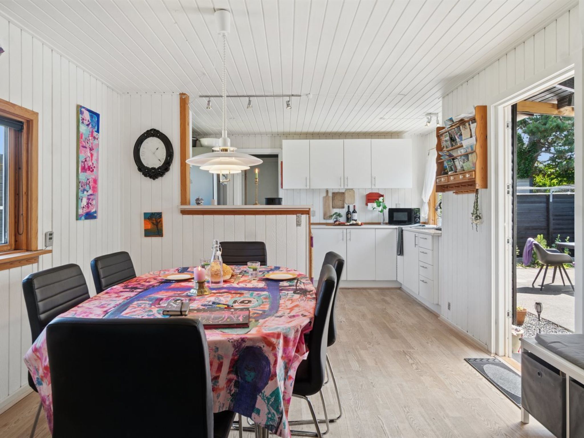 Een eetgedeelte met een tafel voor zes personen, een aangrenzende keuken en uitzicht op de omgeving door een deur.