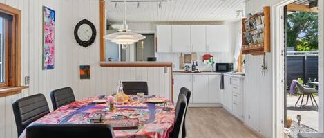 Een eetgedeelte met een tafel voor zes personen, een aangrenzende keuken en uitzicht op de omgeving door een deur.