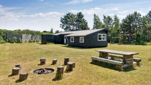 A cabin with a fire pit and picnic table in a grassy field, surrounded by trees.